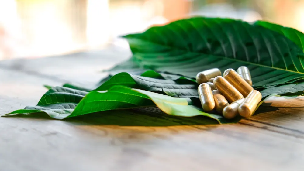 kratom leaves on a table with kratom capsules